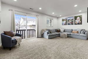 Carpeted living room with recessed lighting, sliding glass door, and baseboards