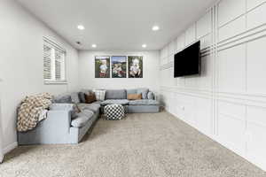 Living area with light colored carpet, recessed lighting, and a decorative wall
