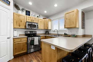 Kitchen featuring appliances with stainless steel finishes, a peninsula, light countertops, vaulted ceiling, and wood floors