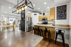 Kitchen featuring appliances with stainless steel finishes, recessed lighting, decorative light fixtures, light countertops, and a breakfast bar