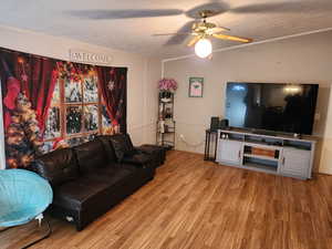 Living area with ceiling fan, wood finished floors, a textured ceiling, ornamental molding, and a decorative wall