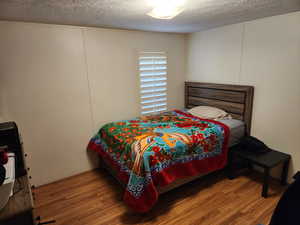 Bedroom with a textured ceiling, wood finished floors, and a decorative wall