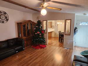 Living room with lofted ceiling, a textured ceiling, light wood finished floors, a ceiling fan, and a chandelier