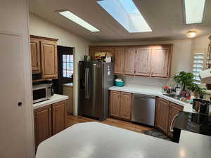 Kitchen with appliances with stainless steel finishes, light countertops, vaulted ceiling, light wood finished floors, and a skylight