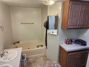 Full bath featuring vanity, a textured ceiling, a tub with jets, and light tile patterned floors