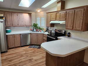 Kitchen featuring appliances with stainless steel finishes, light countertops, a peninsula, light wood-style floors, and under cabinet range hood