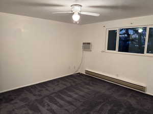 Spare room featuring a baseboard heating unit, dark carpet, ceiling fan, and a wall mounted AC