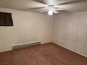 Carpeted spare room featuring a baseboard heating unit, a textured ceiling, and ceiling fan