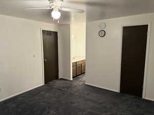 Empty room with dark colored carpet, a textured ceiling, and ceiling fan