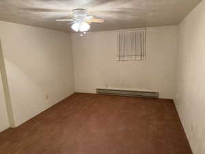 Carpeted empty room with a baseboard radiator, ceiling fan, and a textured ceiling