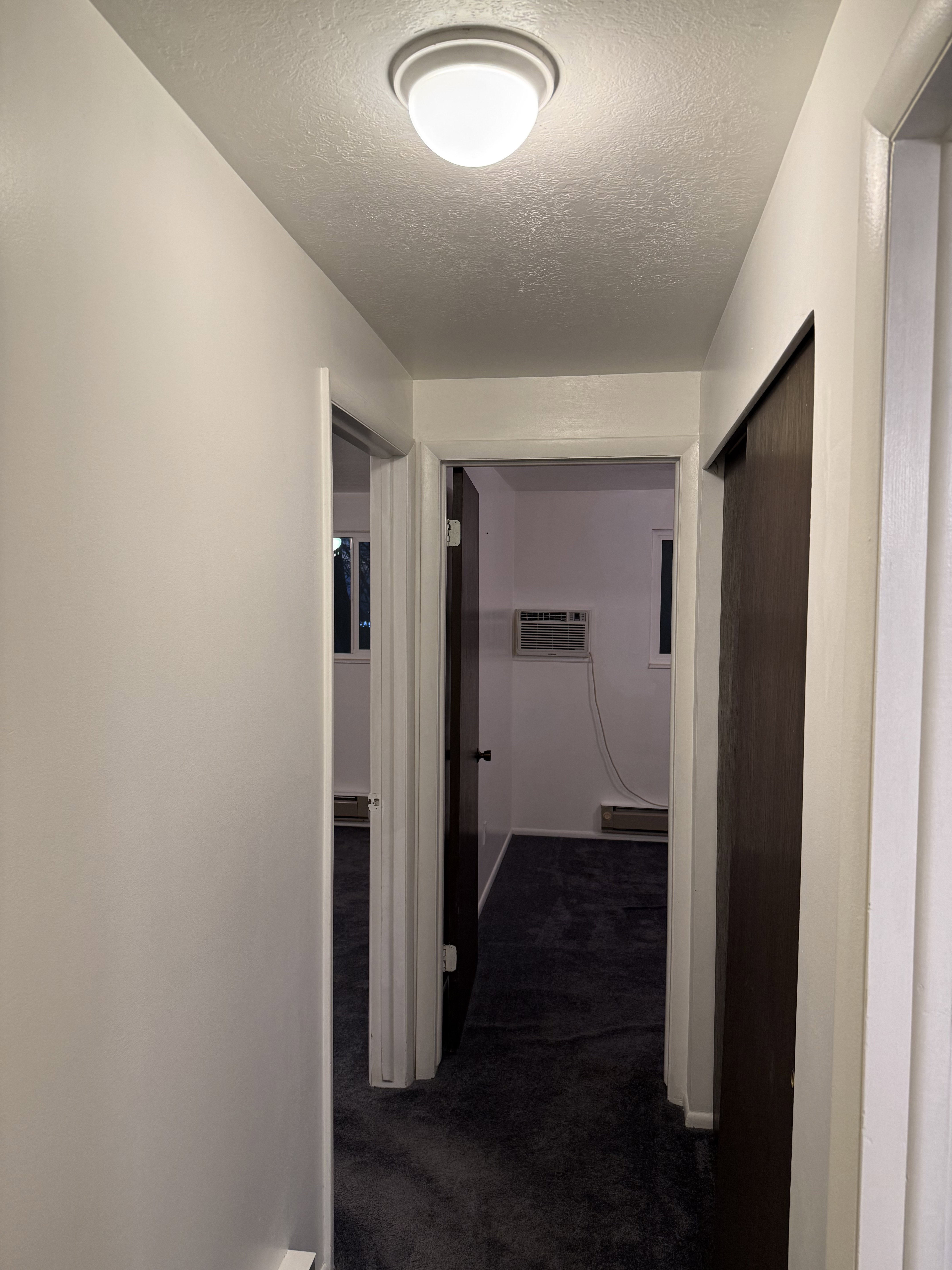 Corridor featuring dark colored carpet, a textured ceiling, and a wall mounted air conditioner