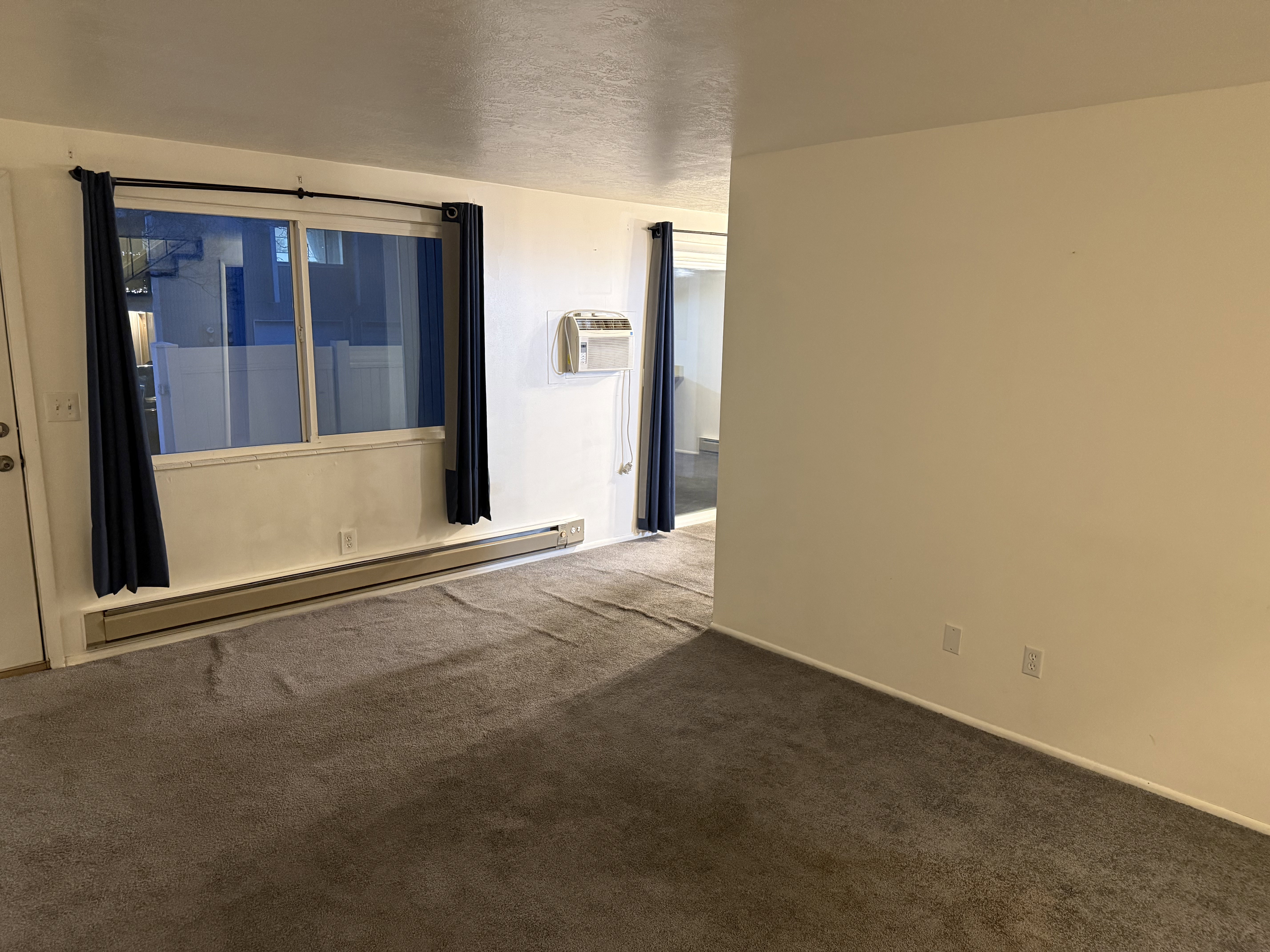 Empty room featuring carpet, a baseboard heating unit, a wall mounted air conditioner, and a textured ceiling