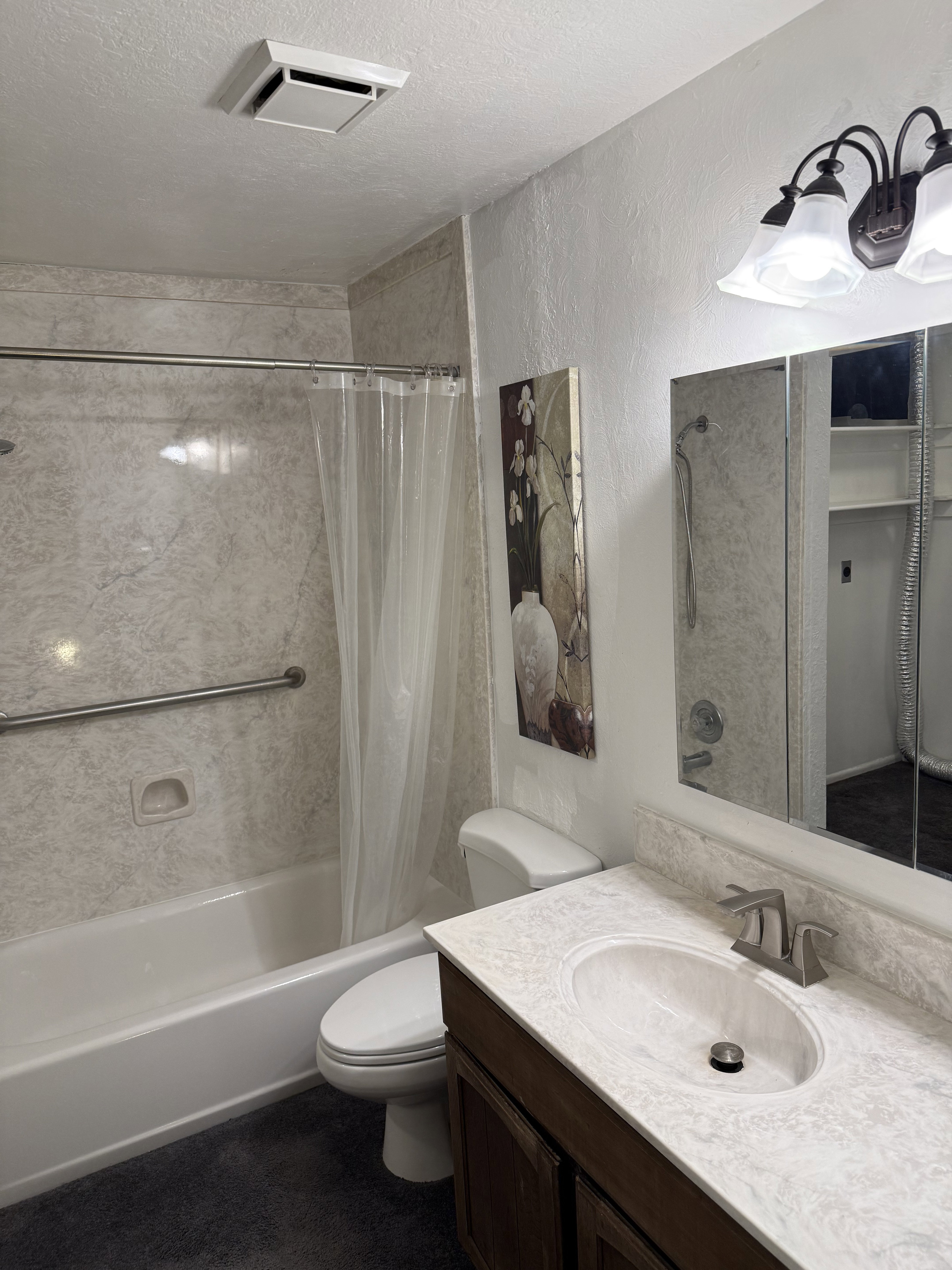 Bathroom with vanity, shower / tub combo, a textured wall, and a textured ceiling