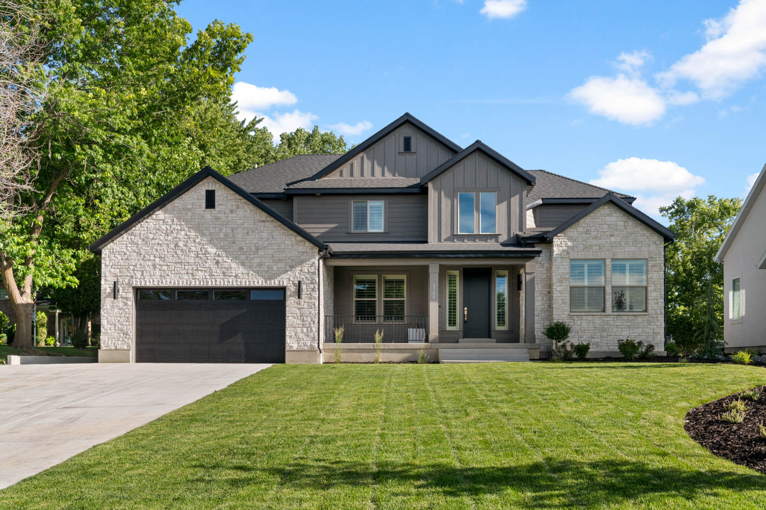 Modern farmhouse-style exterior featuring a striking combination of light-colored stone veneer and dark-toned vertical siding
