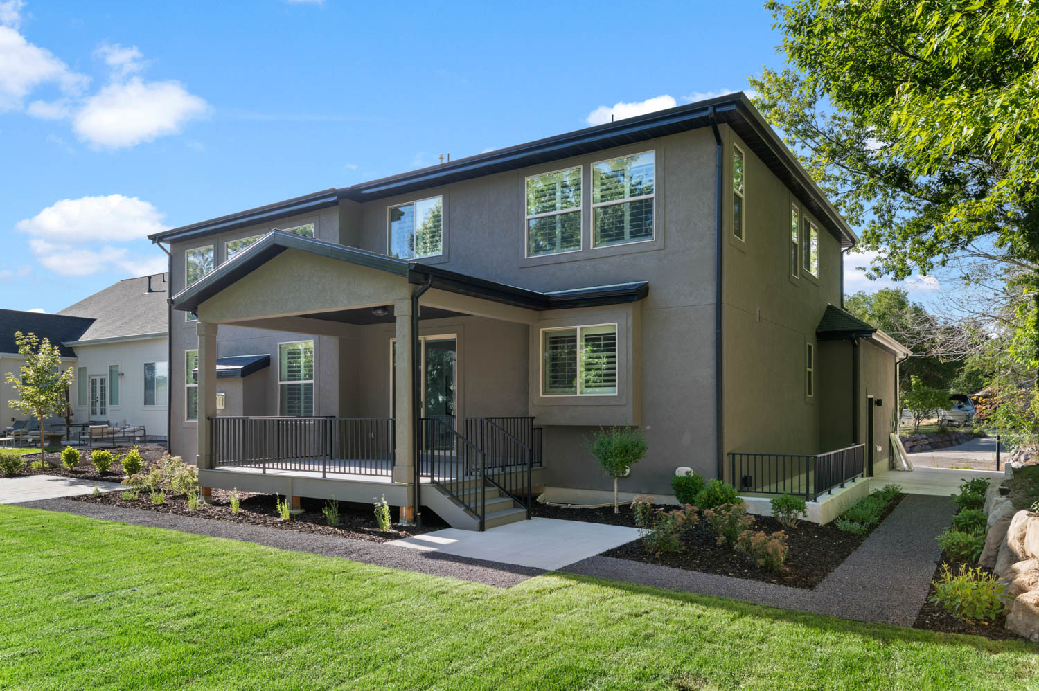 Rear exterior featuring a covered patio, composite deck, stucco siding, and black metal railings