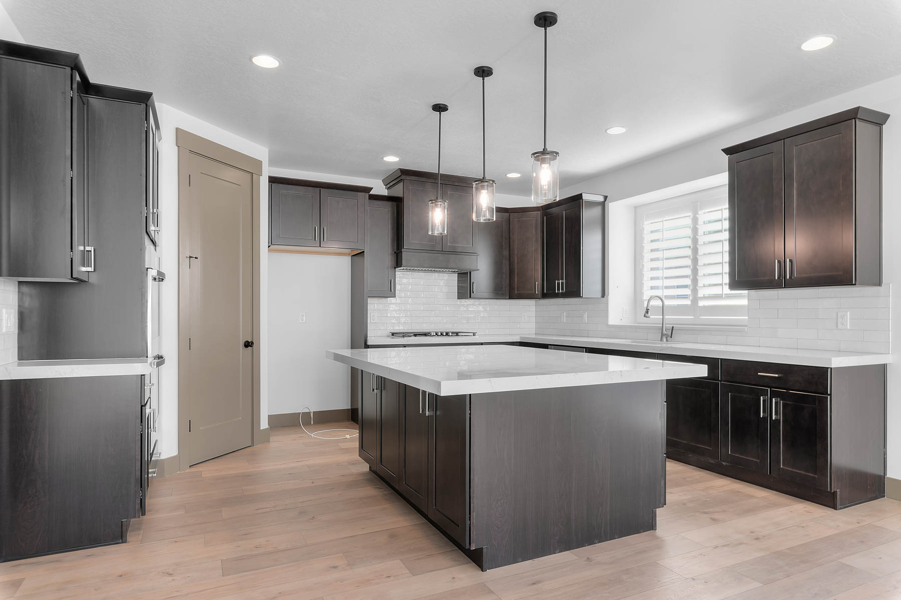 Kitchen with pendant lighting, light wood-type flooring, dark wood finish cabinets, a kitchen island, and light stone counters