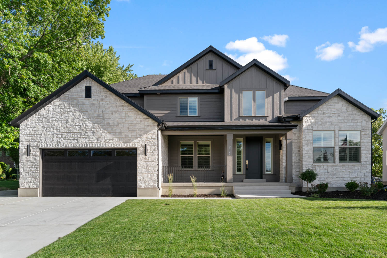 Modern farmhouse exterior featuring a stone and board-and-batten facade, a covered front porch, an attached two-car garage, and a concrete driveway