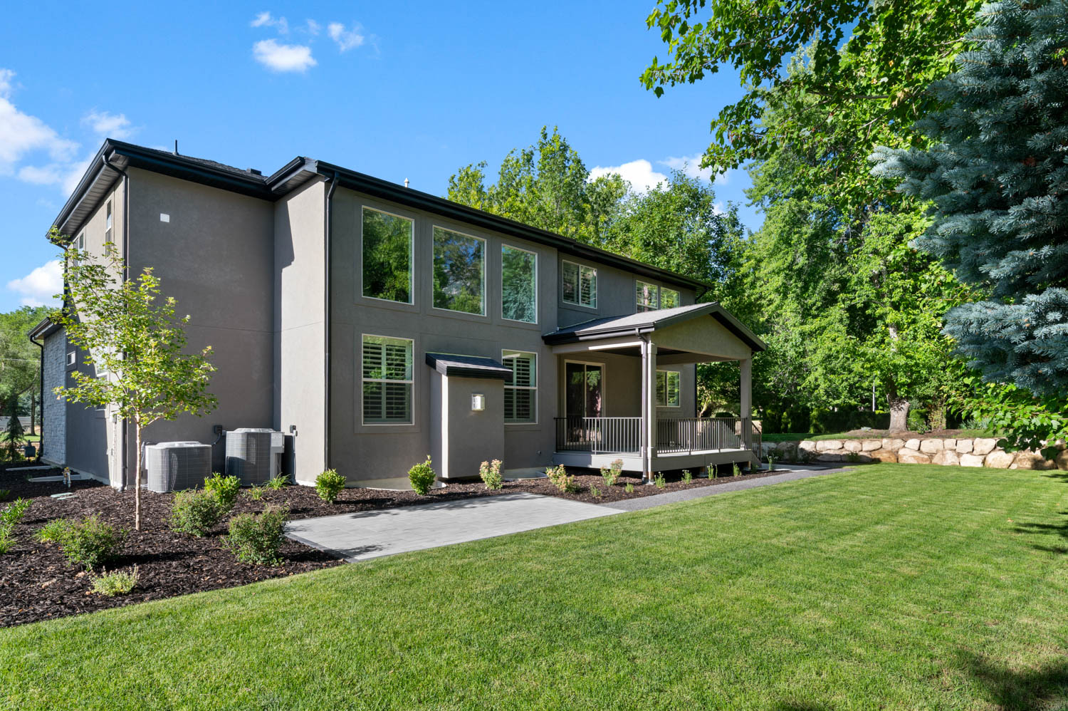 Spacious backyard featuring a covered patio, extensive lawn, mature trees, and a stone retaining wall