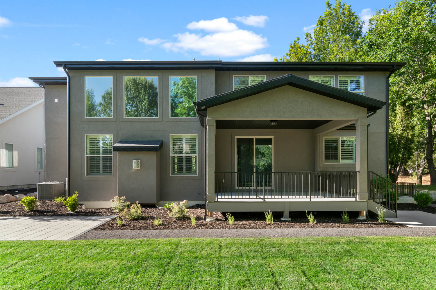 Rear exterior featuring a covered porch with a sliding glass door, black railing, and stairs to grade