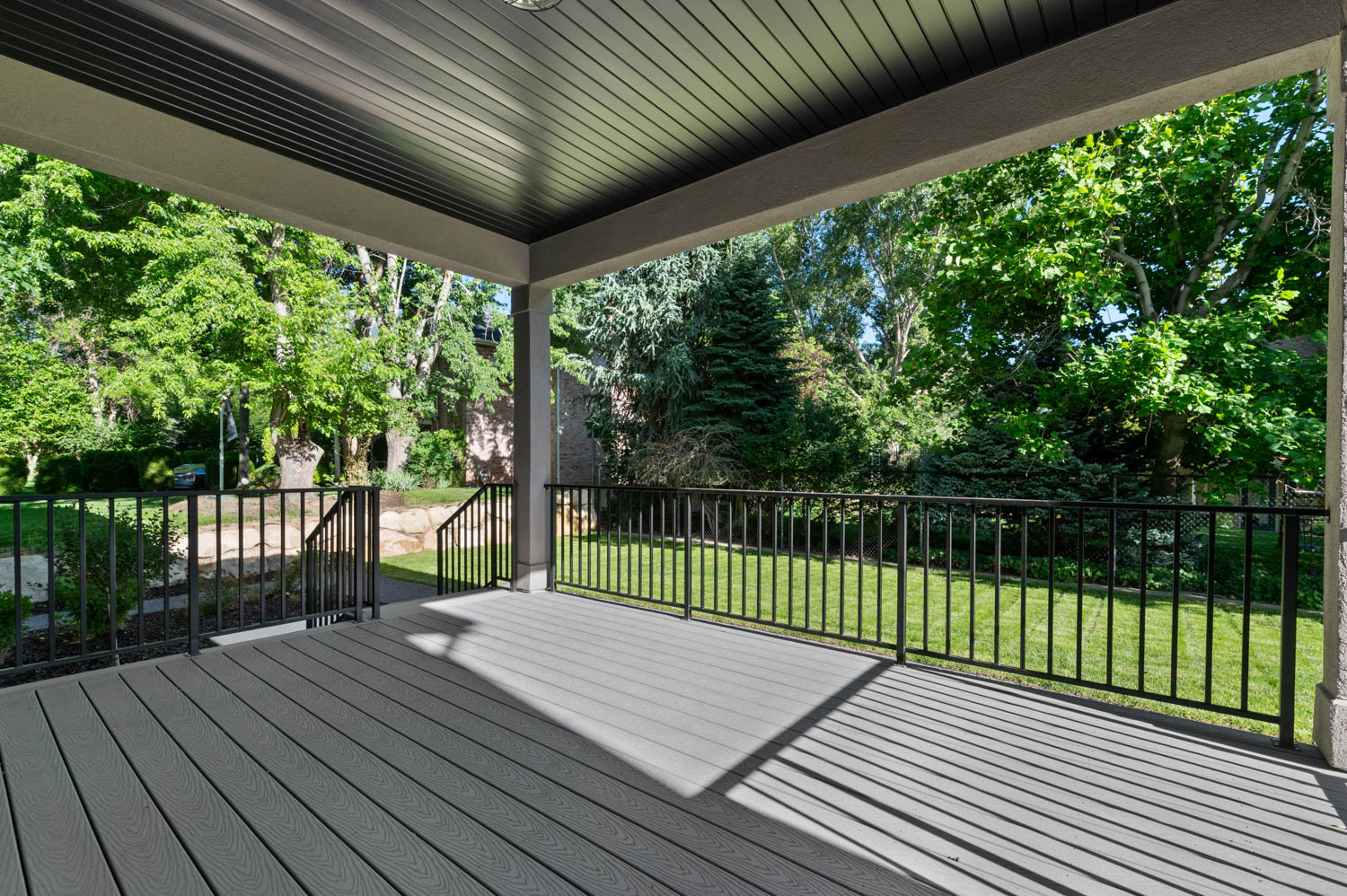 Spacious covered deck featuring composite decking, black metal railings, and an overhead light fixture