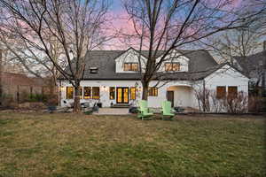 Back of house at dusk with a lawn, a patio, stucco siding, and roof with shingles