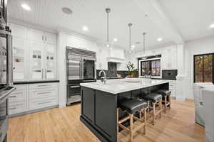 Kitchen with a kitchen bar, stainless steel appliances, light wood-style floors, dark cabinets, and white cabinetry