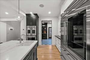 Kitchen with dark cabinets, hanging light fixtures, dark stone counters, stainless steel appliances, and light wood-type flooring