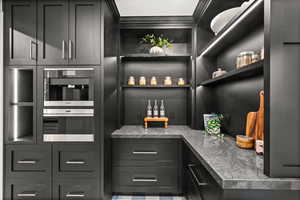 Bar area with open shelves, dark cabinetry, light countertops, crown molding.