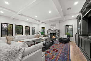 Living area with a high end fireplace, light wood finished floors, beamed ceiling, and recessed lighting