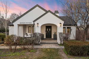 View of front of house with a porch, a chimney, and stucco siding