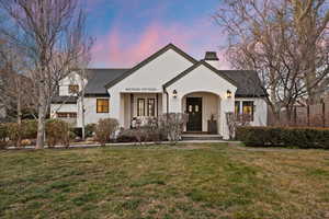 View of front of property featuring a porch, a lawn, a chimney, stucco siding, and a shingled roof