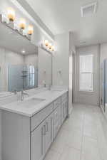 Full bath with a stall shower, double vanity, and light tile patterned floors