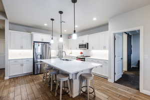 Kitchen featuring a kitchen bar, white cabinets, stainless steel appliances, a barn door, and a kitchen island with sink