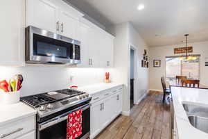 Kitchen with appliances with stainless steel finishes, white cabinetry, decorative light fixtures, light wood-type flooring, and recessed lighting
