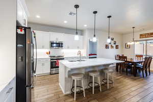 Kitchen with appliances with stainless steel finishes, a kitchen breakfast bar, white cabinetry, wood finish floors, and recessed lighting