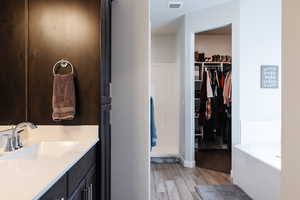 Bathroom with a garden tub, a walk in closet, vanity, and light wood-style flooring