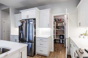 Kitchen with stainless steel appliances, white cabinets, light wood-style flooring, and light stone countertops