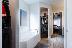 Full bathroom with a garden tub, a spacious closet, light wood-style floors, ensuite bathroom, and ceiling fan