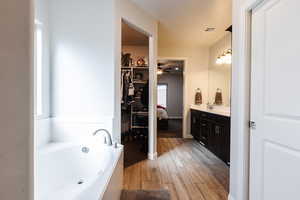 Full bathroom featuring a bath, vanity, light wood finished floors, a spacious closet, and ceiling fan