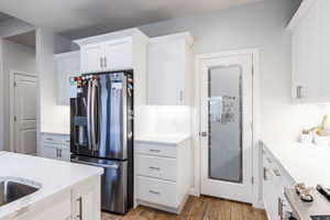 Kitchen with stainless steel appliances, white cabinets, light wood-style flooring, and light stone counters
