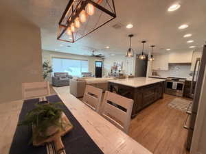 Kitchen with dark brown cabinetry, pendant lighting, appliances with stainless steel finishes, light wood-type flooring, and backsplash