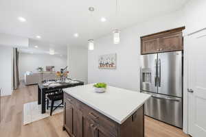 Kitchen featuring dark brown cabinetry, stainless steel refrigerator with ice dispenser, pendant lighting, a kitchen island, and light wood finished floors