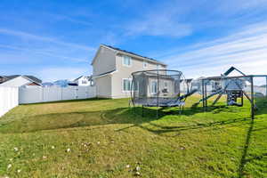 Back of property featuring a trampoline, a playground, a gate, stucco siding, and a fenced backyard