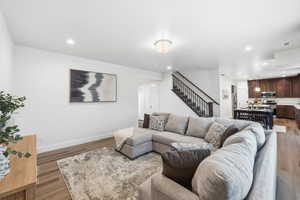 Living room with wood finished floors, recessed lighting, and stairway