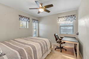 Bedroom with ceiling fan, an office area, and light colored carpet