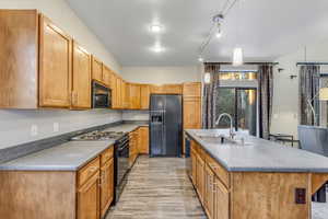 Kitchen with black appliances, a kitchen island with sink, pendant lighting, brown cabinets, and light wood-style floors