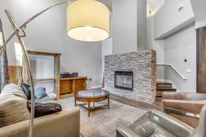 Living room featuring a towering ceiling, wood finished floors, a stone fireplace, and stairs
