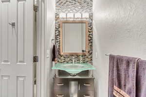 Half bath featuring a textured wall, decorative backsplash, and vanity