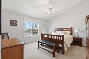 Owners suite,  with vaulted ceiling, light colored carpet, and ceiling fan