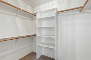 Owners suite walk in closet with dark colored carpet